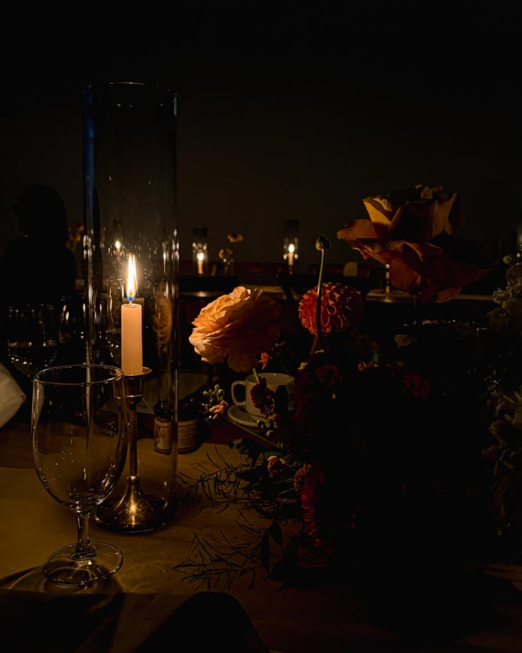 A head-on shot shows a dark table scene with a candle and flower arrangement.