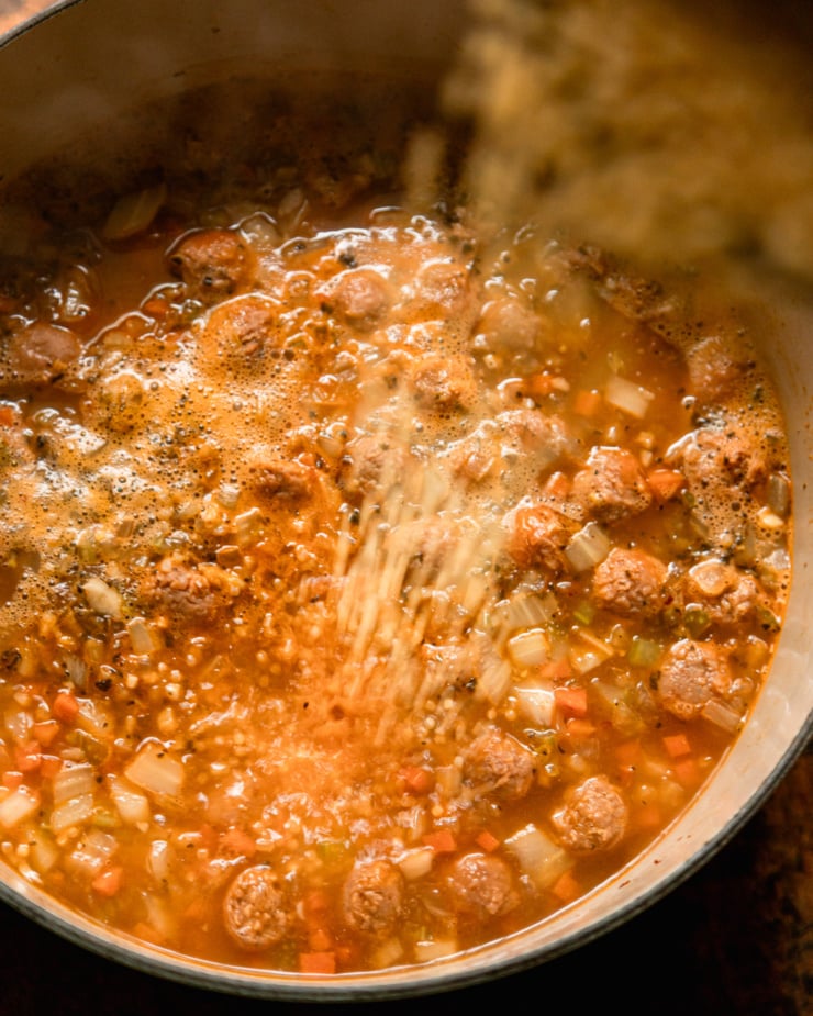 An overhead shot shows tiny pasta being poured into a pot of simmering soup.