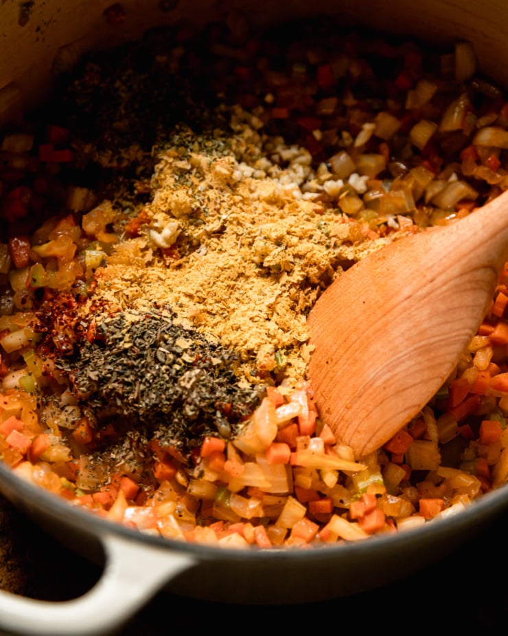 A slight 3/4 angle shot shows sautéed vegetables in a pot with nutritional yeast and dried herbs sprinkled on top.