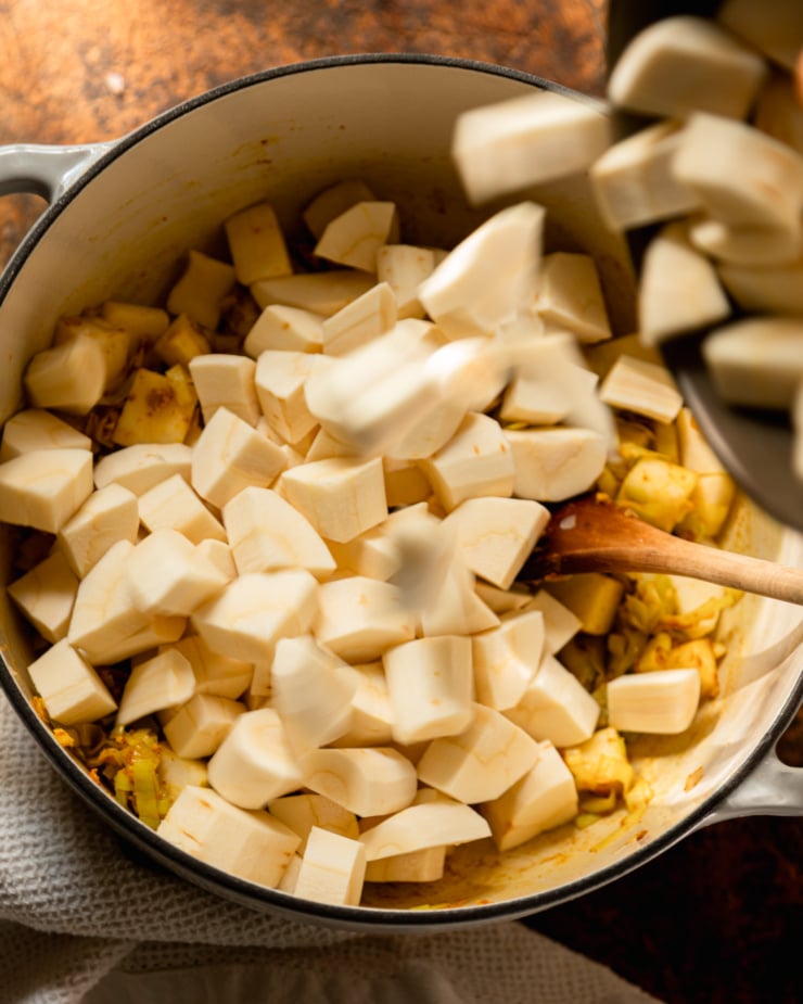 An overhead shot shows chopped parsnips being poured into a big Dutch oven pot.