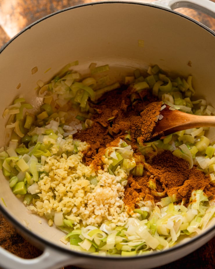 An overhead shot shows sautéed leeks in a pot with ginger, garlic, and curry powder added.