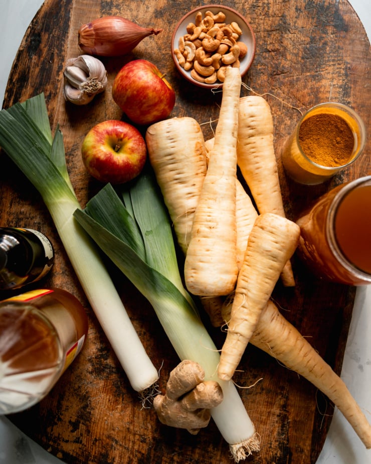 An overhead shot shows ingredients needed for a hearty vegan soup, all on a worn wood cutting board.