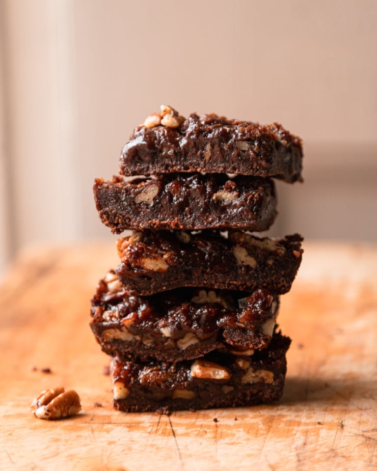 A head-on shot shows a stack of chocolate pecan bars on a wood cutting board.