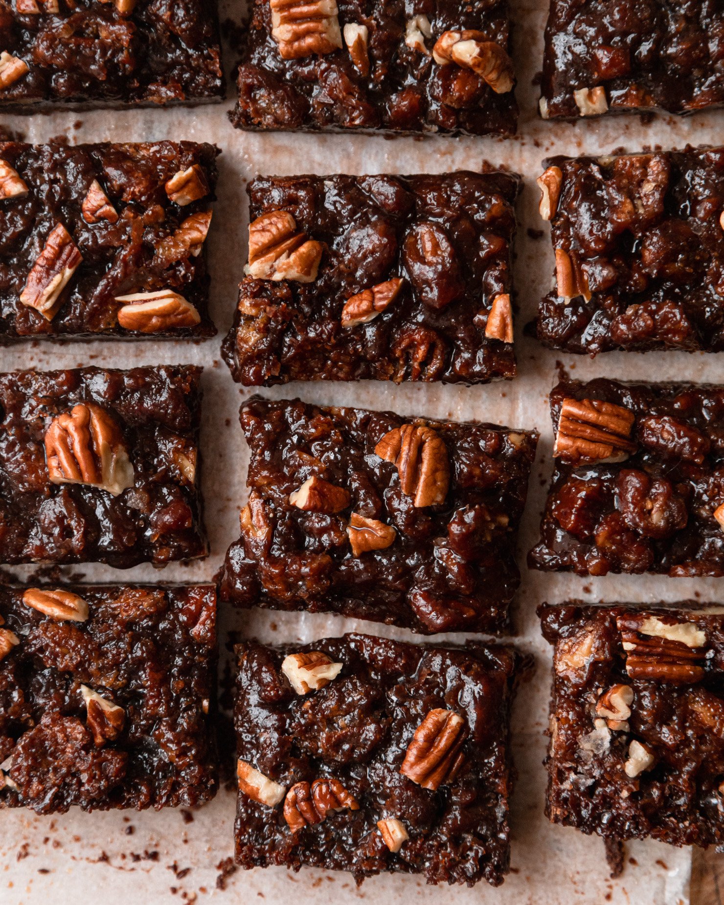 An overhead shot shows gooey chocolate pecan bars on top of parchment paper.