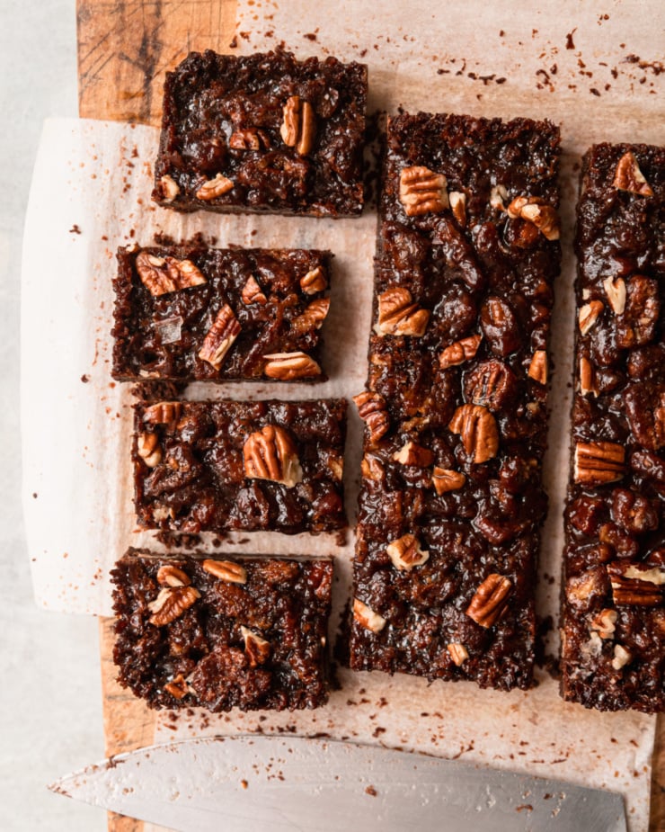 An overhead shot shows chocolate pecan bars in the process of being cut. A knife is seen nearby.