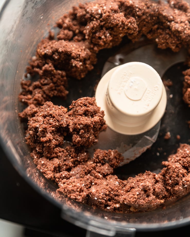 An overhead shot shows a gluten-free and vegan chocolate crust mixture for bars in a food processor.