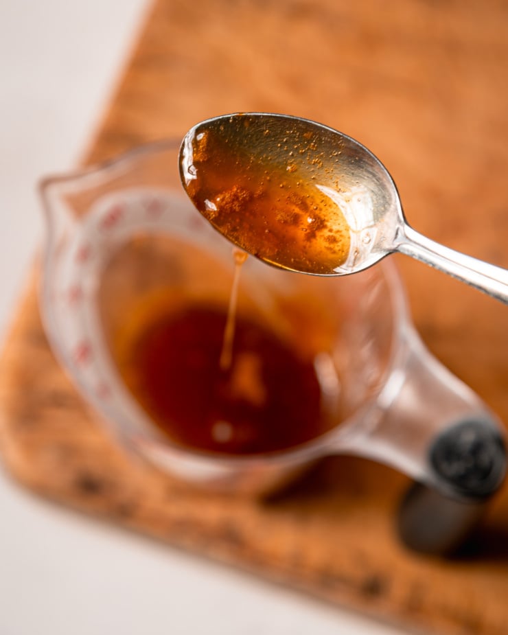 An overhead shot shows a spoon dripping apple cider reduction into a measuring cup.