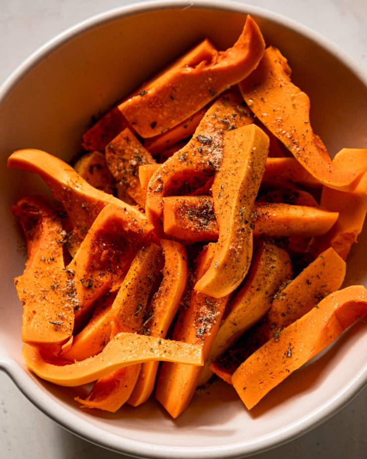 An overhead shot shows raw honeynut squash wedges in a bowl, topped with olive oil and herb salt.