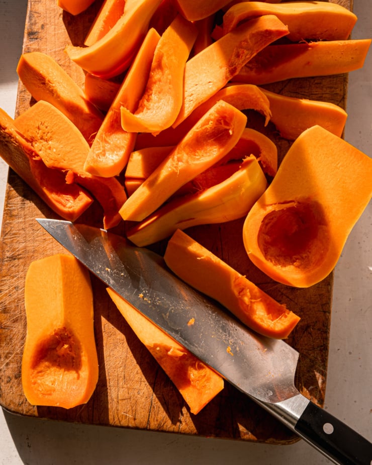 An overhead shot shows a cutting board with a bunch of cut honeynut squash on it and a chef's knife.