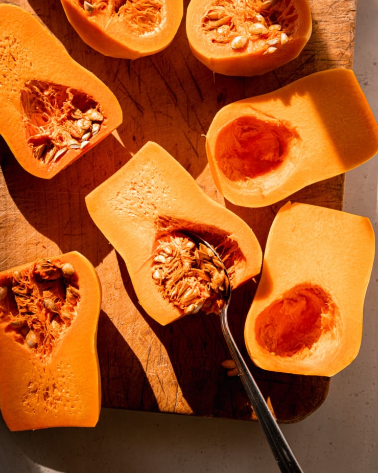 An overhead shot shows little squash halves on a cutting board. Some halves have their seeds scooped out. A spoon is sticking out of the seedy area of one half.