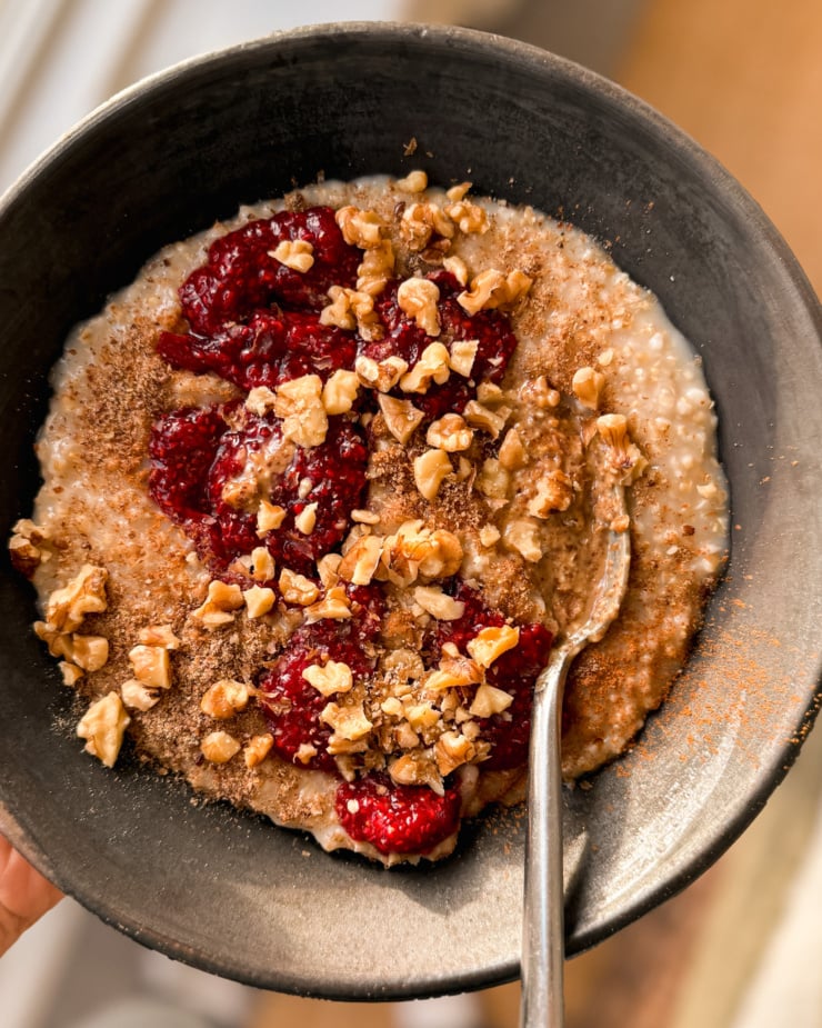 An overhead shot shows a bowl of steel cut oat porridge topped with chia jam and walnuts.