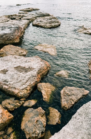An overhead shot shows big rocks at the shore of a lake.