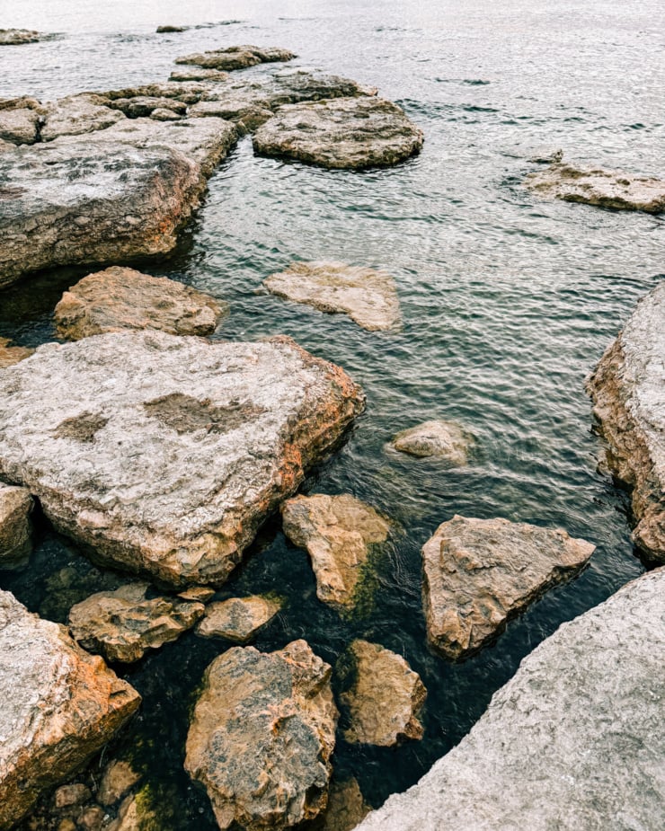An overhead shot shows big rocks at the shore of a lake.