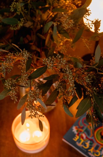 An overhead shot shows some seeded eucalyptus branches in a vase, backlit by glowing candlelight.