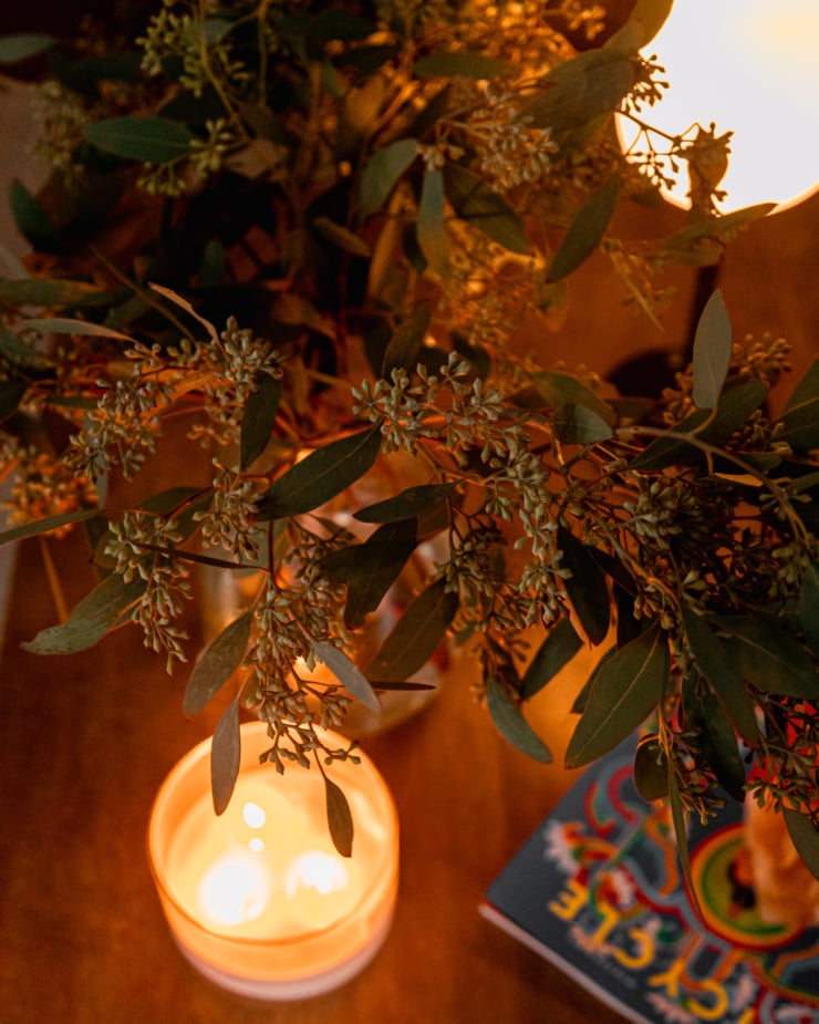 An overhead shot shows some seeded eucalyptus branches in a vase, backlit by glowing candlelight.