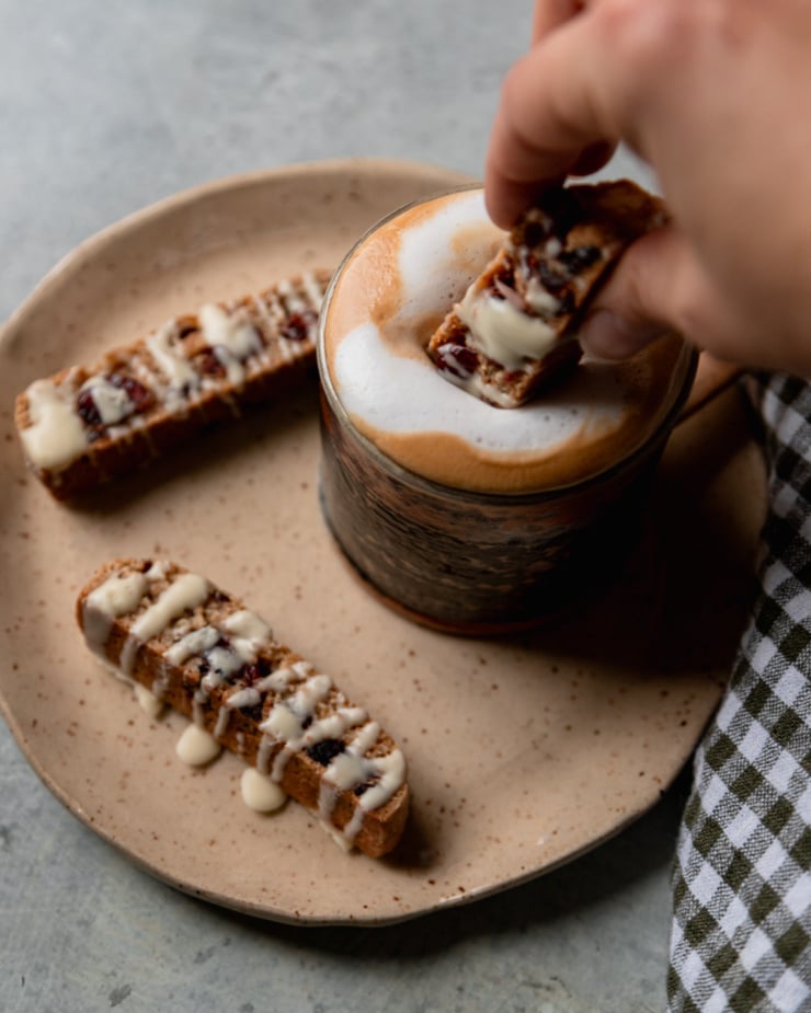 A 3/4 angle image shows a hand dunking a biscotti into a frothy coffee.