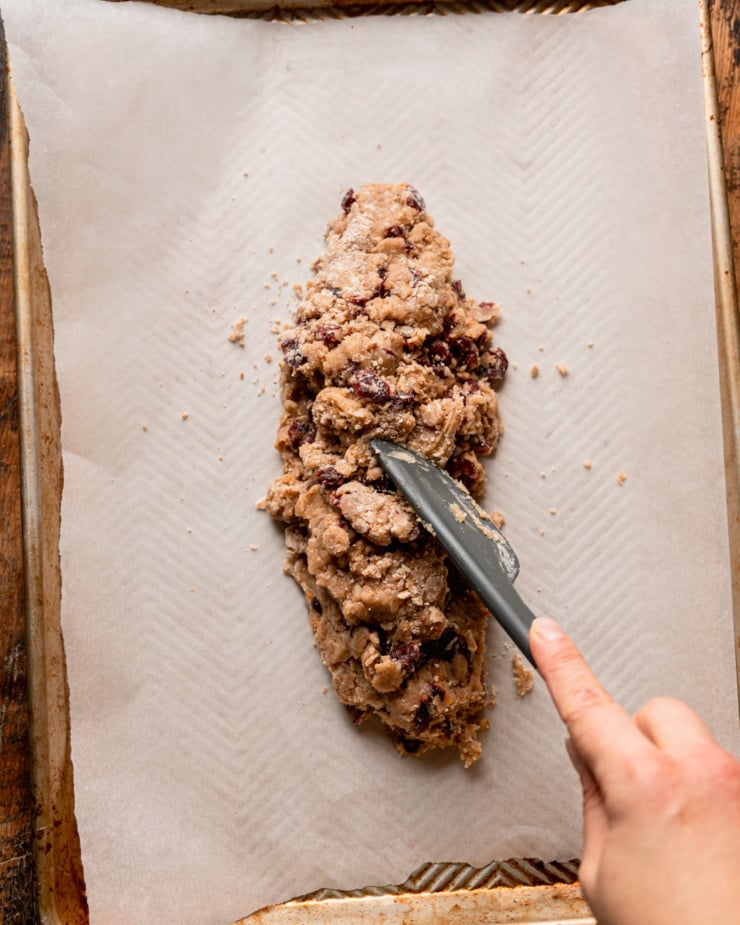 An overhead shot shows a hand using a spatula to transfer cookie dough to a baking sheet.