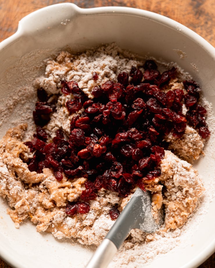 An overhead shot shows cookie batter in a bowl with a bunch of dried cranberries added on top.
