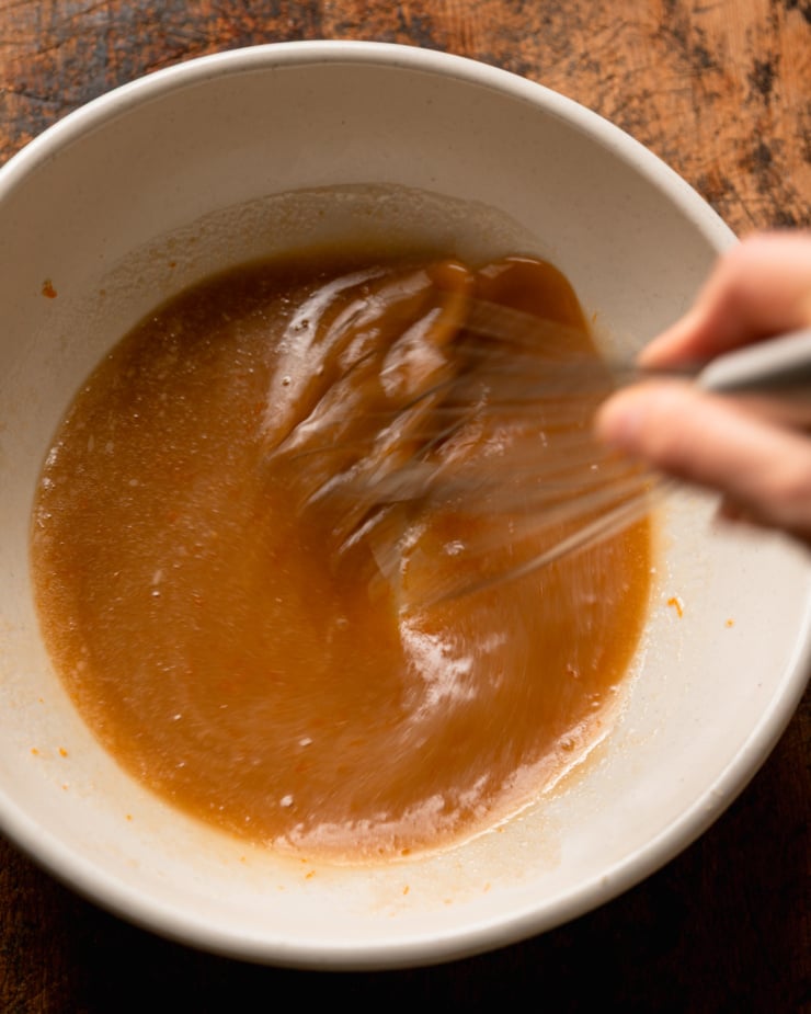 An overhead shot shows a hand using a whisk to bring some liquid ingredients together in a bowl.