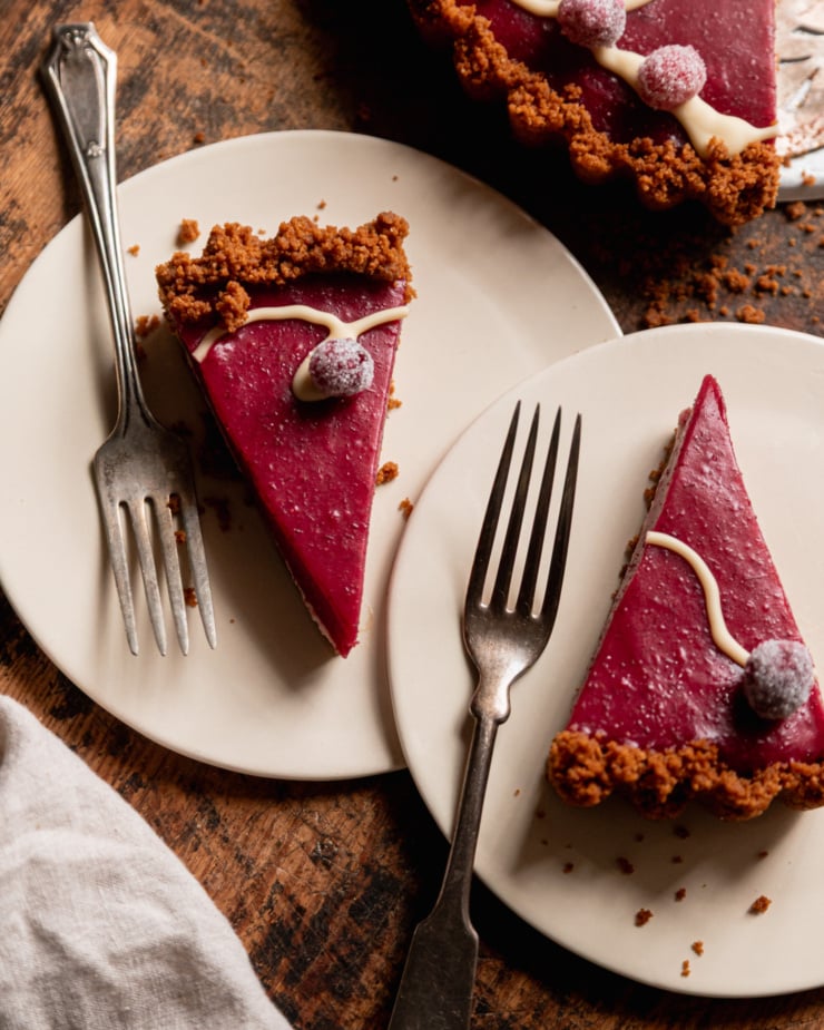 An overhead shot shows two slices of vegan cranberry tart on two small dessert plates with forks to the side.
