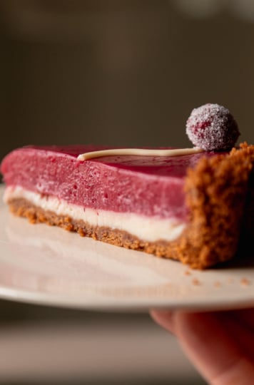 An up close, head-on shot shows a slice of vegan cranberry tart on a plate with two defined layers: white chocolate and cranberry curd.