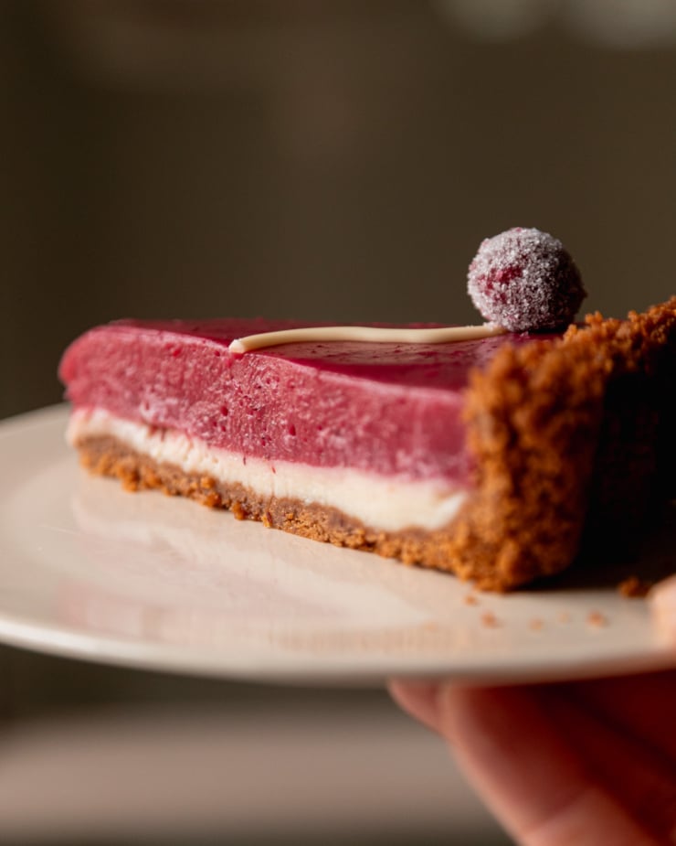 An up close, head-on shot shows a slice of vegan cranberry tart on a plate with two defined layers: white chocolate and cranberry curd.