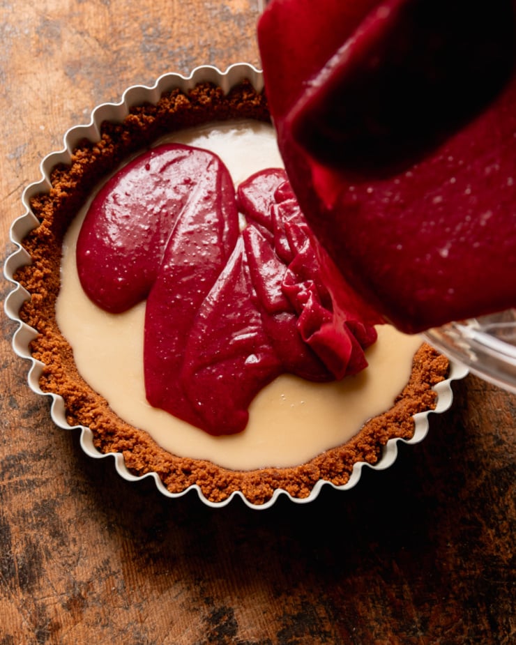 An overhead shot shows cranberry curd being poured over a white chocolate layer in a tart.