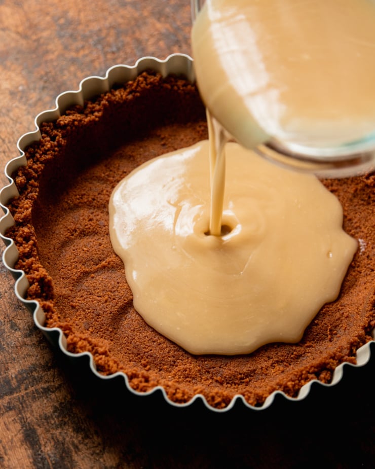 A 3/4 angle image shows a melted white chocolate mixture being poured into a Biscoff cookie crust in a tart pan.