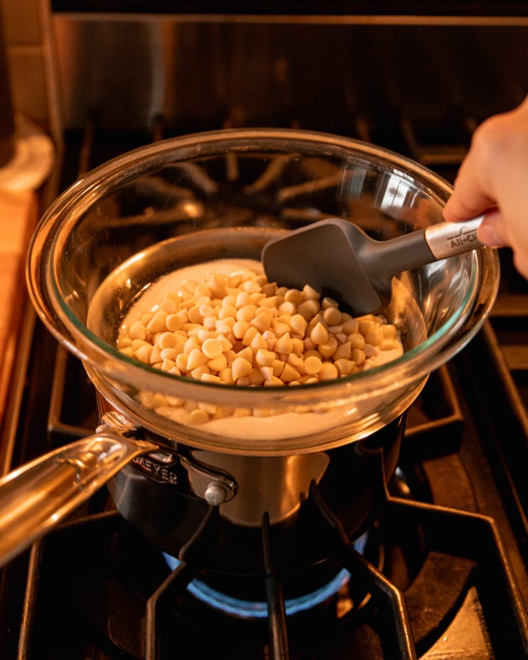 A slight 3/4 angle shot shows a double boiler setup on the stove with some white chocolate chips melting.