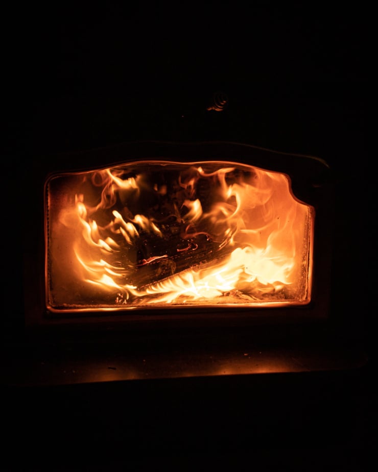 A head-on shot shows a roaring fire inside of a wood stove.