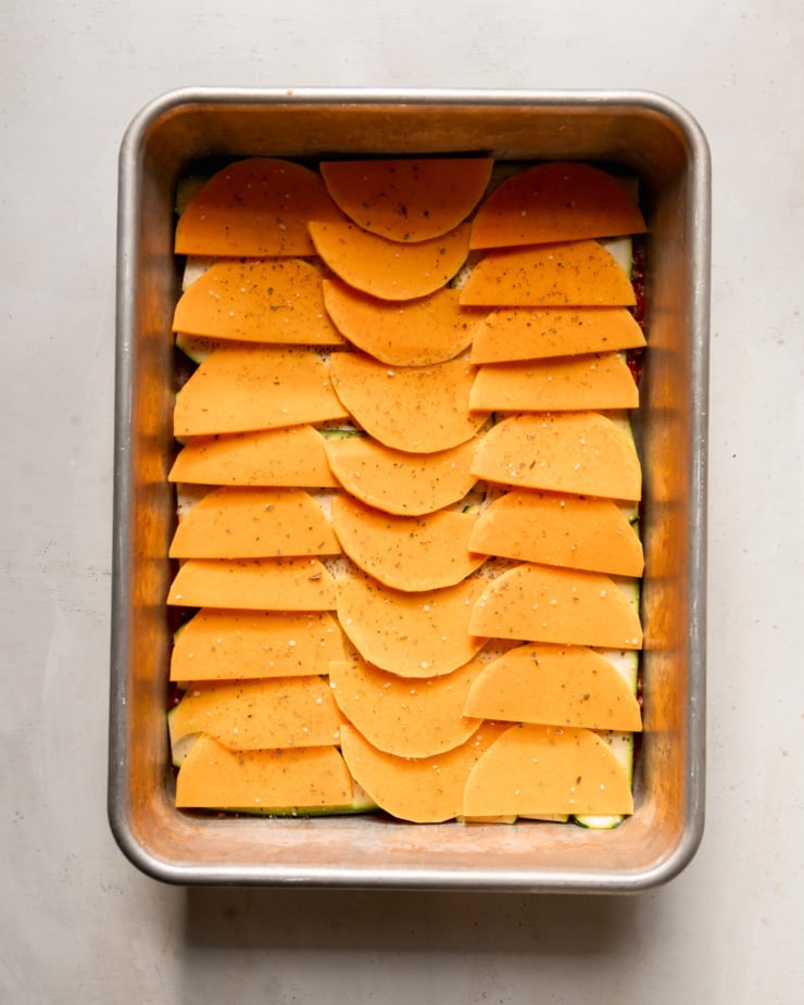 An overhead shot shows thinly sliced butternut squash in a baking dish.