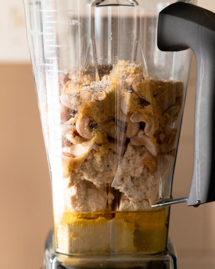 A head-on shot shows ingredients for a vegan "ricotta" in an upright blender pitcher.
