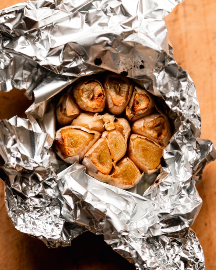 An overhead shot shows a foil-wrapped head of garlic that has been roasted. The cloves are exposed and golden.