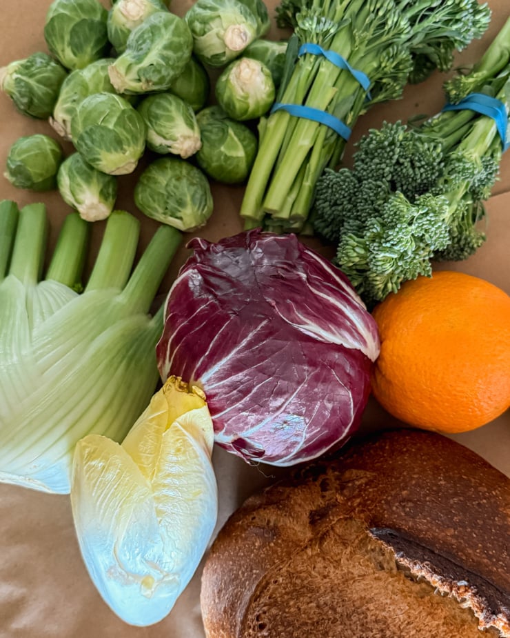 An overhead shot shows some vegetables, oranges, and a loaf of sourdough bread.