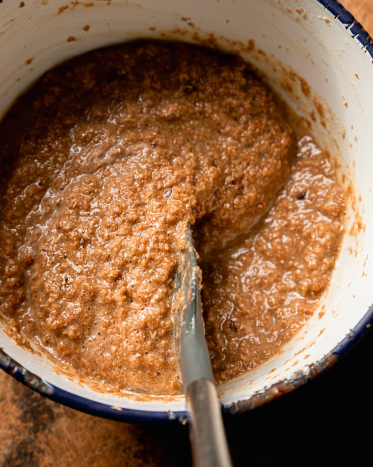 An up close, overhead shot shows the mixed wet ingredients for a batch of vegan bran muffins. A spatula is stirring them together.