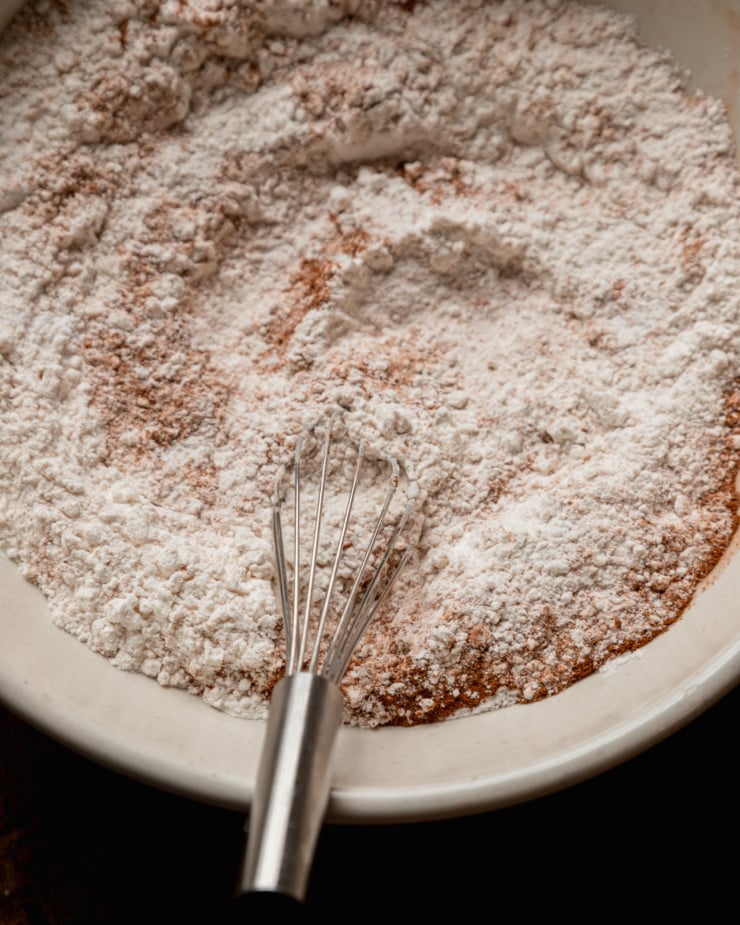 An overhead shot shows dry ingredients and a whisk in a wide mixing bowl.