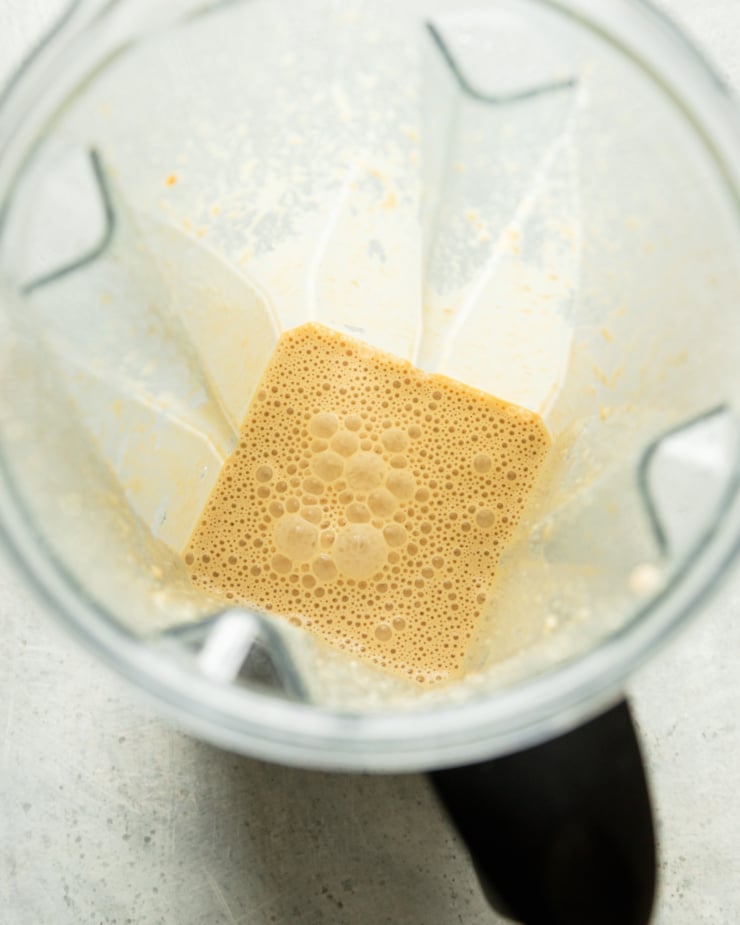 An overhead shot shows a blended vegan "cream" of cashews, nutritional yeast, miso, and vegan Worcestershire sauce in a blender jar.