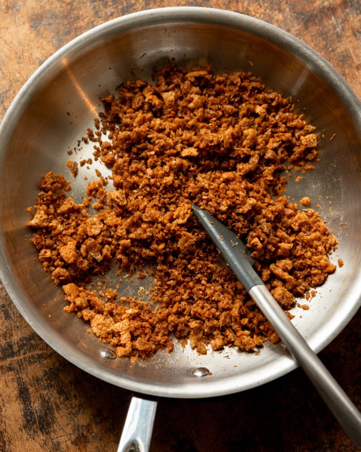 An overhead shot shows toasted seasoned bread crumbs in a skillet. A spatula is set into the skillet also.