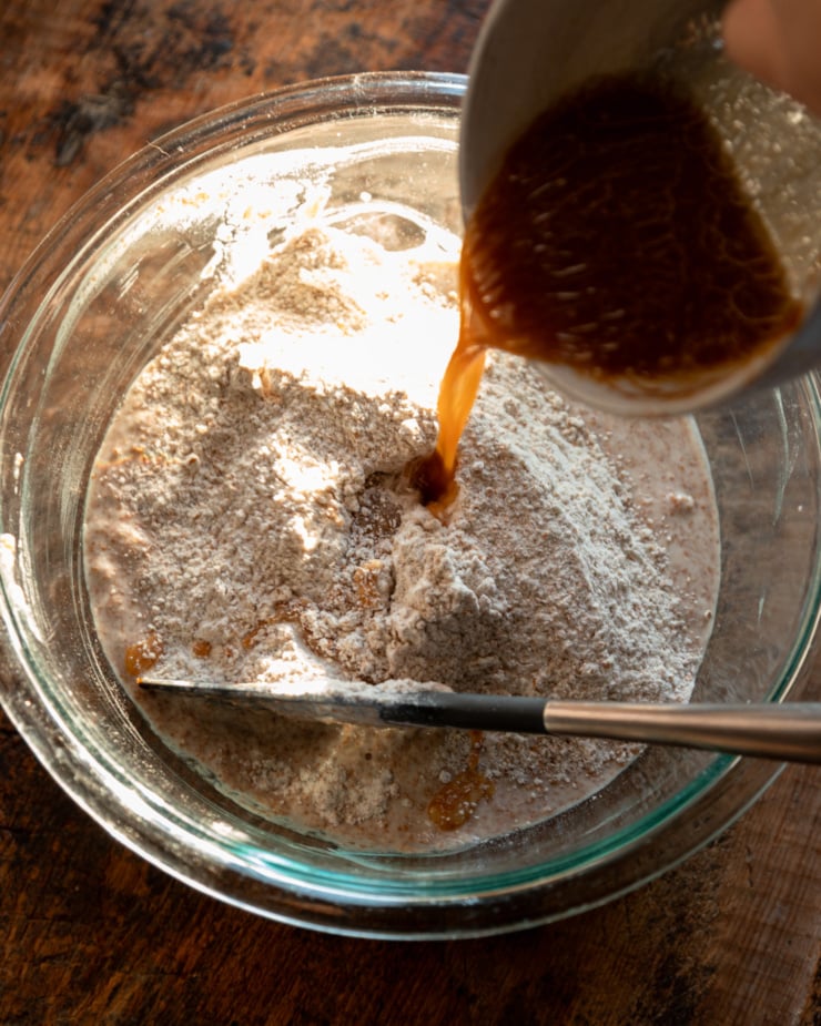 An overhead shot shows a molasses and water mixture being poured into a bowl with flour and water.